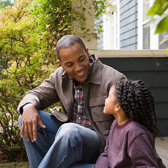 Father and young daughter sitting on a porch talking