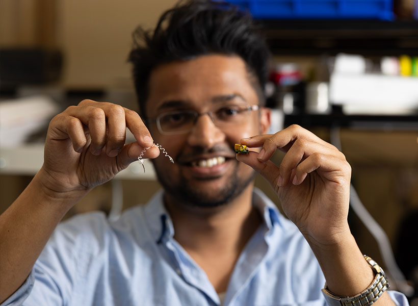 Man smiles at camera while holding up tiny devices. 