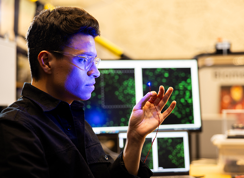 Man holds a fiber that is illuminated with blue light at its tip.